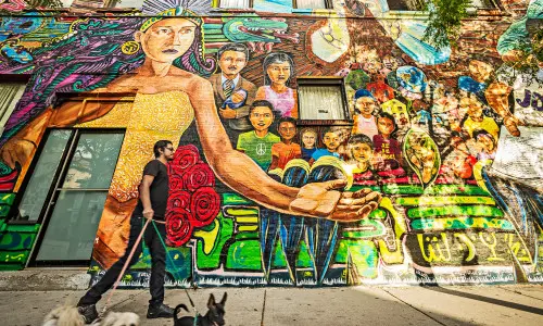 カラフルな壁画の前で3匹の犬を散歩させる男。