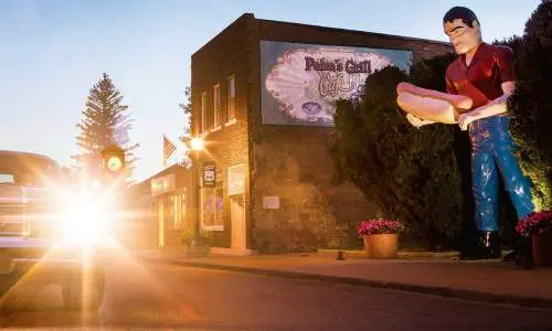 ホットドッグを持った巨大な銅像のある車の後ろに沈む夕日