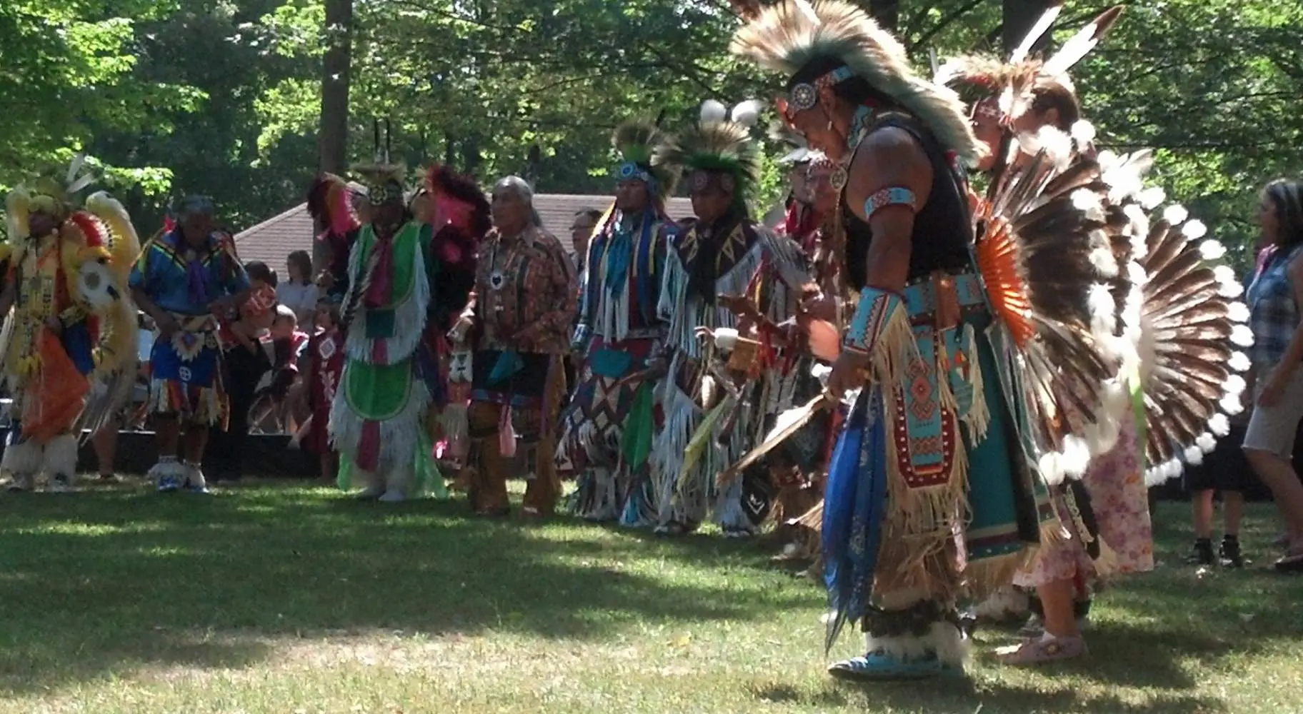 木々が生い茂る草原で、ネイティブ・アメリカンの衣装をまとった男たち。