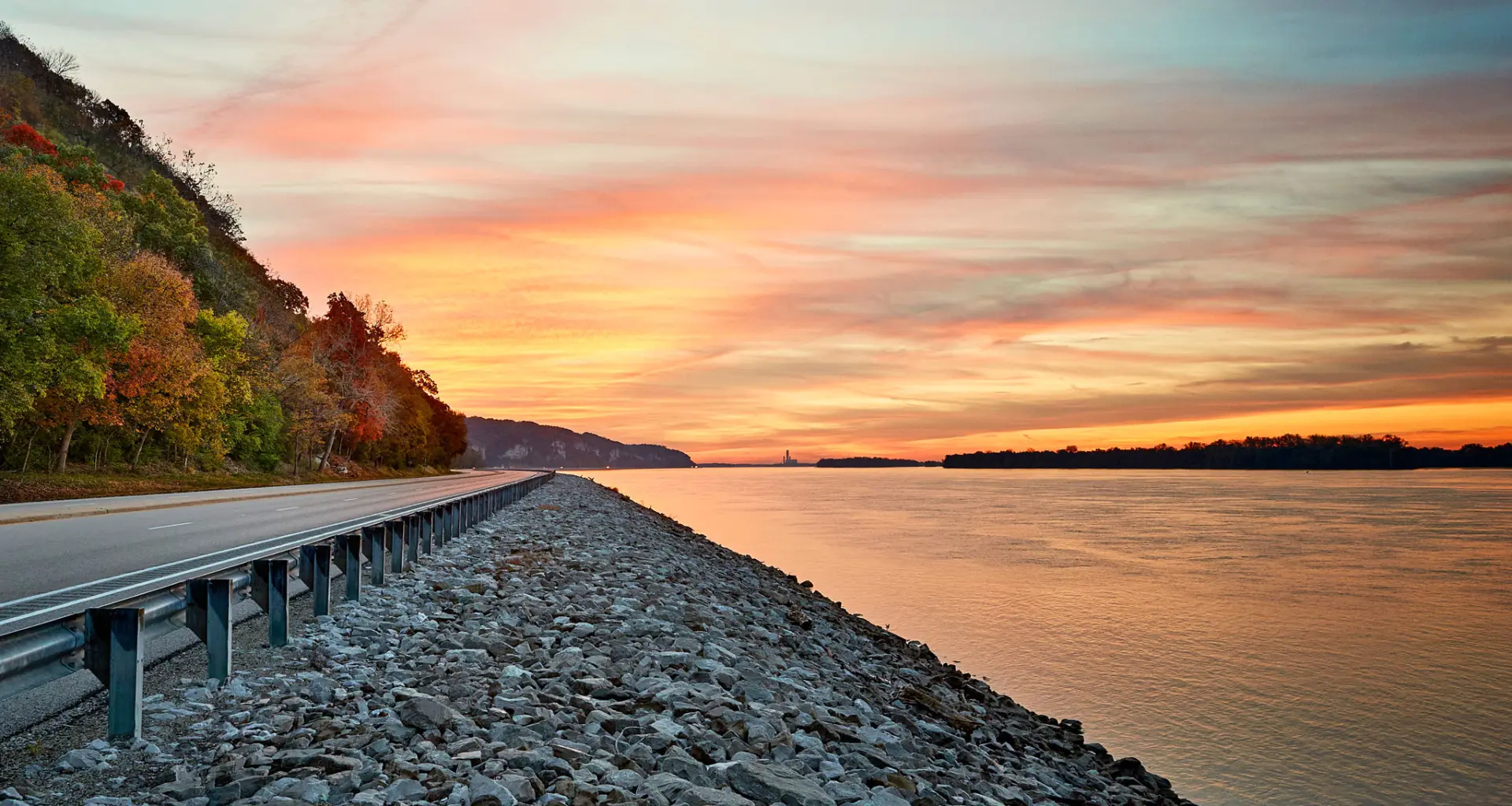 水面に沈む夕日と川沿いの道