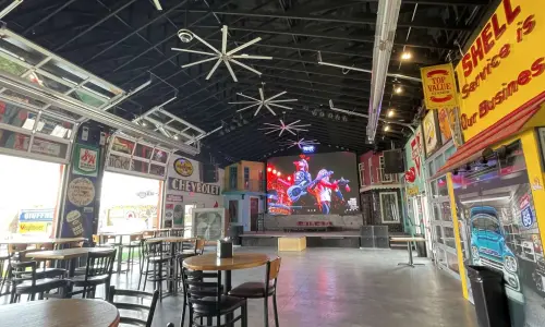 広々としたバー兼ライブハウス。店内にはテーブルが置かれ、ヴィンテージの自動車の看板や装飾が施され、ステージの上には大型スクリーンが設置されている。